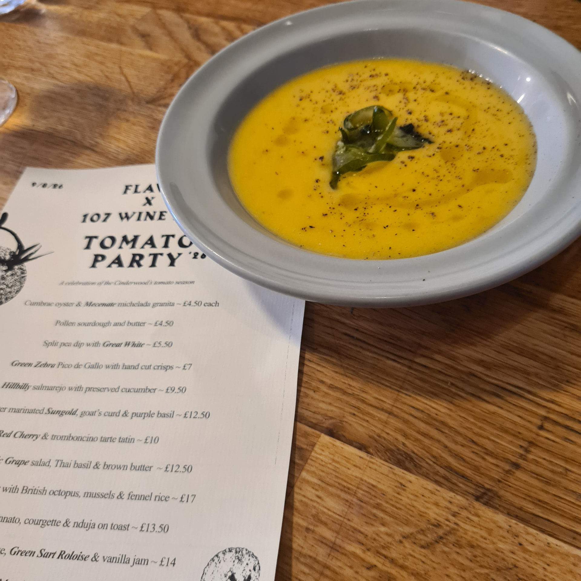 A bowl of chilled yellow tomato salmorejo, dusted with pepper, beside the party menu