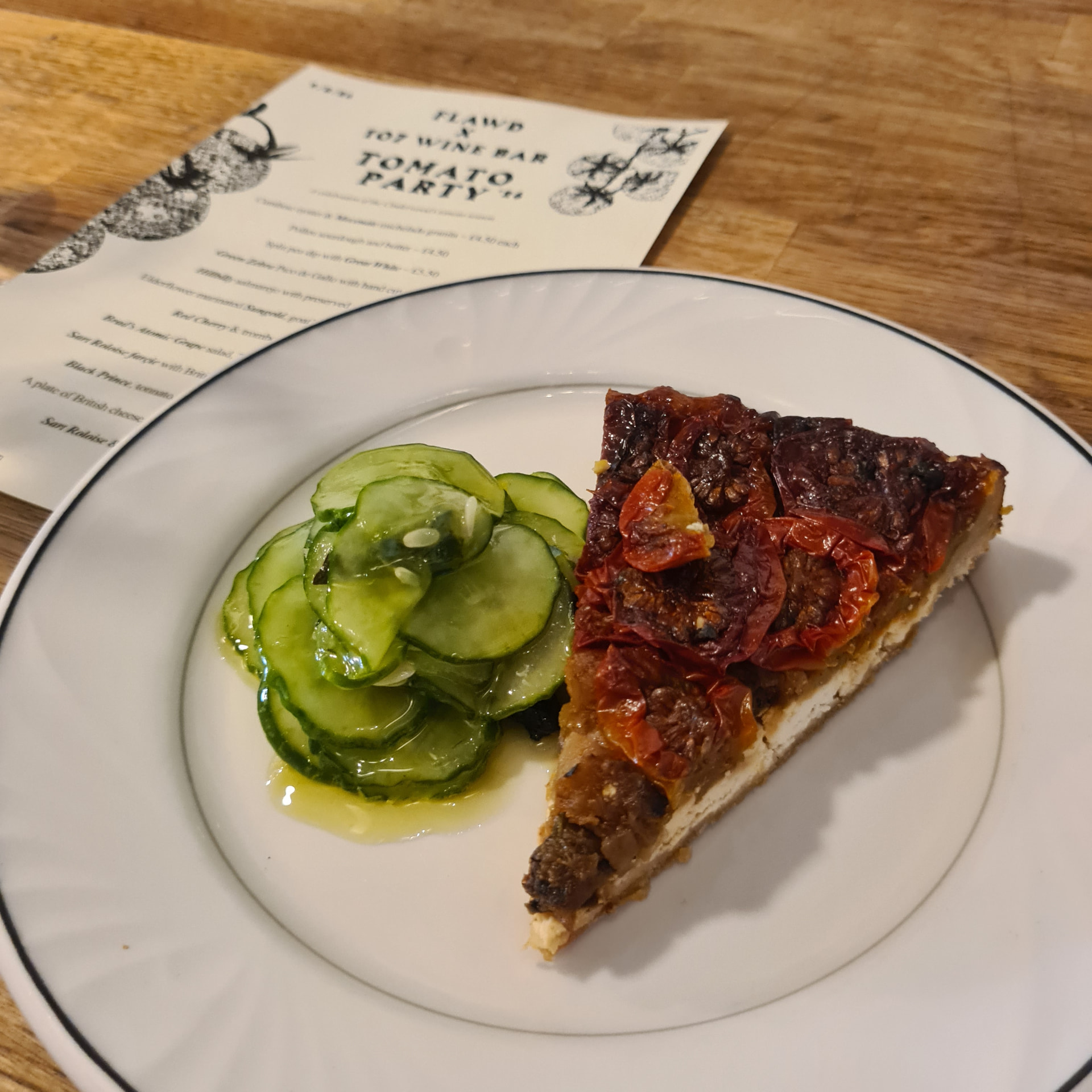 A slice of tomato tarte tatin with preserved cucumber on a white plate